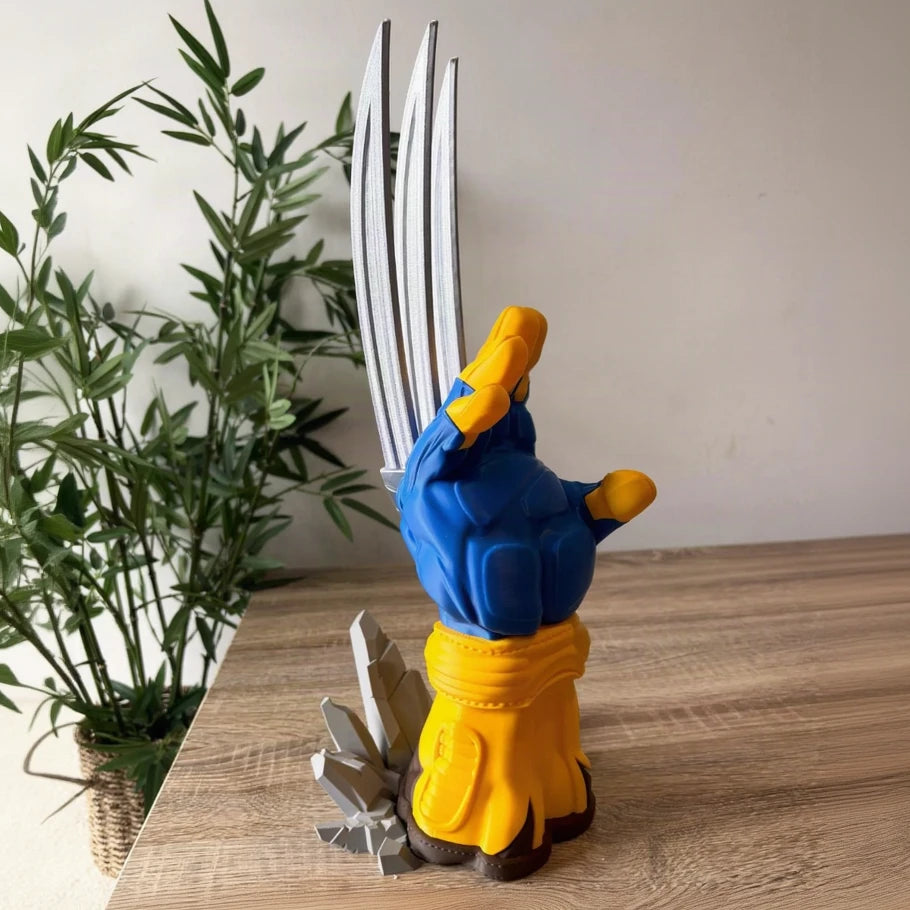 a wolverine collectible figurine standing on a wooden tabletop, with a potted plant and neutral wall in the background. the figurine features blue and yellow armor with silver metallic claws and a gray cracked base.