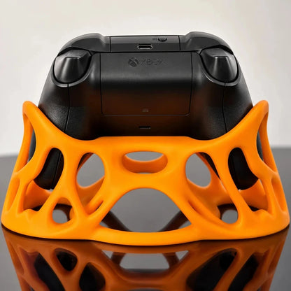 Rear view of an orange Xbox controller stand holding a black Xbox controller, showcasing its ergonomic grips and lattice structure