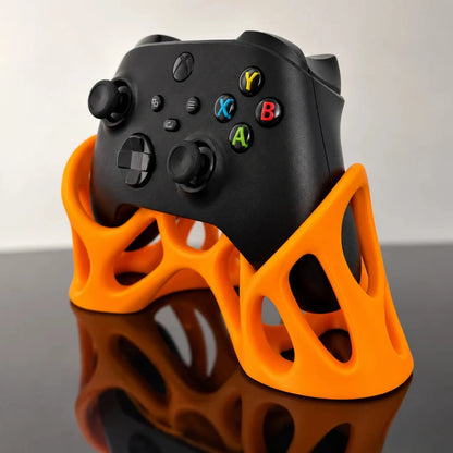 Angled view of a black Xbox controller displayed in an orange 3D-printed controller stand with an open geometric design