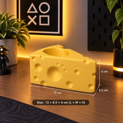 A yellow cheese-shaped desk accessory with a circular cutout on top, shown on a wooden tabletop with dimension labels reading 12 cm, 6 cm, and 8.5 cm.