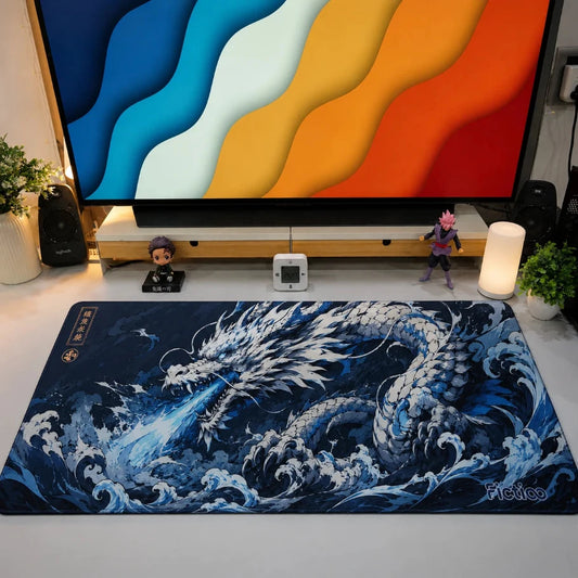 A large rectangular gaming desk mat featuring a detailed blue and white dragon illustration inspired by Japanese wave art, styled on a light gray tabletop in front of a TV stand with a glowing TV, small figurines, and a lamp.