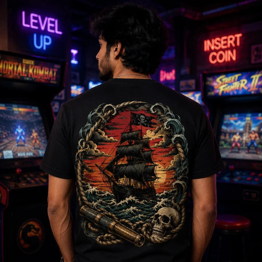 a man viewed from behind wearing a black t-shirt with a large, detailed pirate ship graphic on the back, set in a neon-lit arcade room.