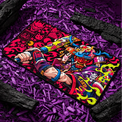 Neon Oni Samurai gaming deskmat featuring vibrant Japanese-inspired artwork in pink, blue, green and red on a black base, displayed on purple wood chips.

