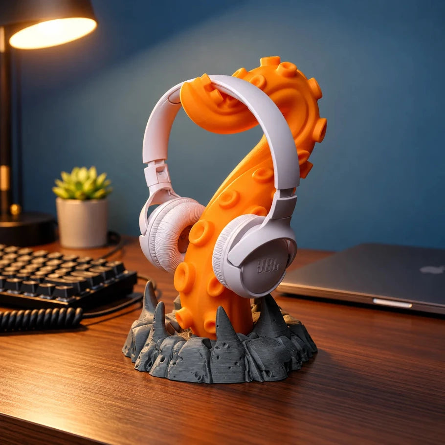 Orange tentacle headphone stand with white JBL headphones and dark grey rocky base on a gaming desk.