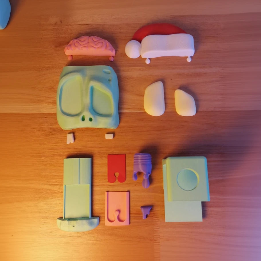 Open view of a zombie headphone stand with a pink brain, bulging eyes, and a slime-dripping red tongue, next to a white Xbox controller on a desk in parts disassembled