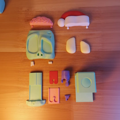 Open view of a zombie headphone stand with a pink brain, bulging eyes, and a slime-dripping red tongue, next to a white Xbox controller on a desk in parts disassembled