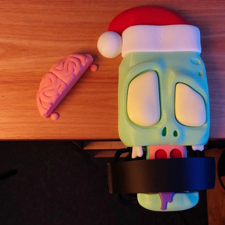zombie headphone stand wearing a red and white santa hat, brain topper removed and placed beside it, black headphones mounted on the tongue."