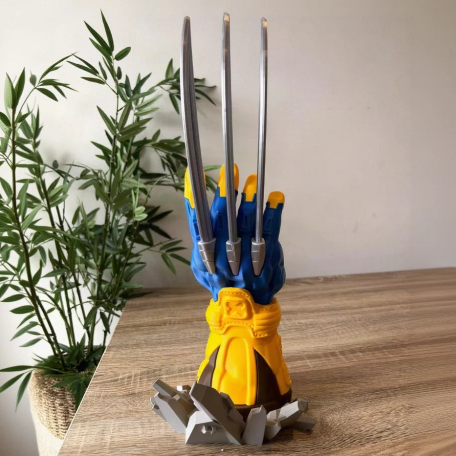 a clawed glove stand or display holder on a wooden tabletop, with a blue glove, yellow wrist area, and four metallic silver claws extending upward. a plant and plain wall are visible in the background.