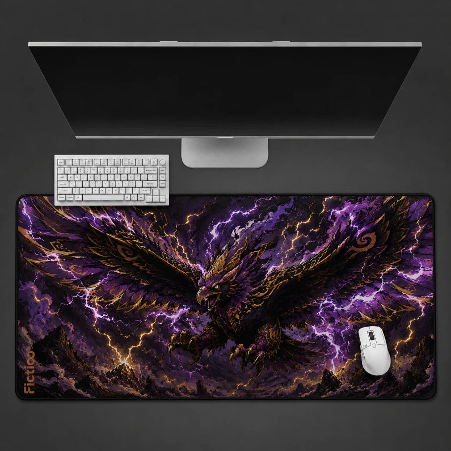 a large desk mat with a dramatic fantasy illustration of a golden eagle surrounded by purple lightning, shown under a computer monitor with a keyboard and mouse on a dark gray background.